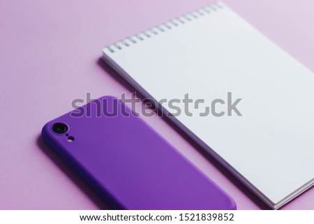A notebook and a smartphone on a light background. Purple silicone case for smartphones.