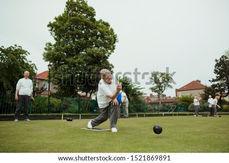 A front view shot of a senior woman taking her shot in a game of lawn bowling.