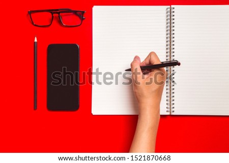 Office supplies on red background with notebook, glasses, pencil, cellphone, handwriter. Space for text.