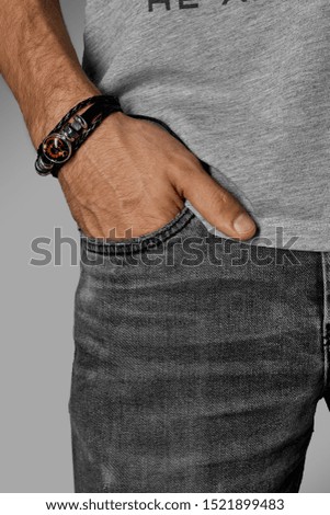 Cropped close-up shot of a male wrist with a multilayer leather bracelet made of leather braids and a strip with metal charms and a circle onlay with a zodiac sign under the glass dome. 