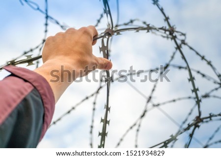 A man's hand is holding the barbed wire on the fence. Escape concept