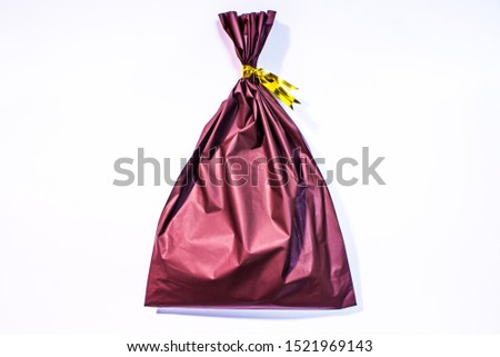 Small wrapped bag with gift. The bag in image is tied with golden ribbons, isolated on white background.