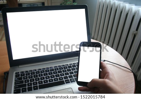 Close up of man using blank cell phone and laptop sending massages shopping online. The man works at the computer and receives the business phone.