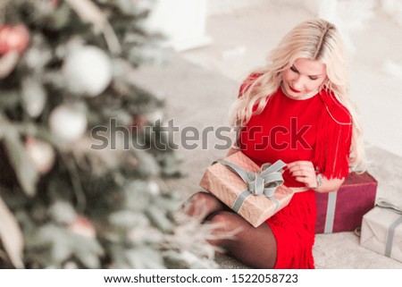 Beautiful girl in a red dress sits with a Christmas gift near the Christmas tree