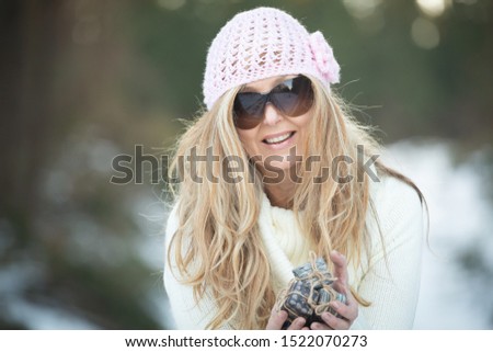 Woman holding little wrapped gifts tied with string in a snowy landscape backdrop. Shallow dof with focus to face only.