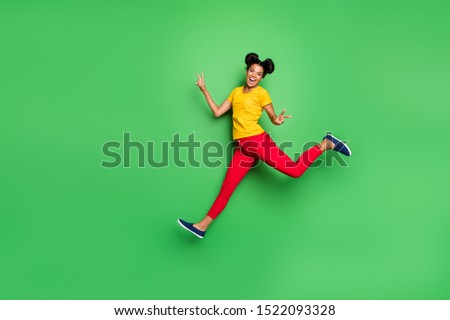 Full body photo of nice dark skin lady jump high running competition participant came first to finish show v-signs wear yellow t-shirt red pants isolated green background