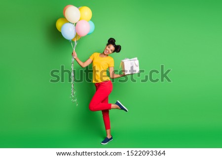 Full length photo of pretty dark skin lady holding air balloons big giftbox birthday party best guest wear casual yellow t-shirt red pants isolated green background