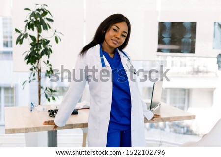 Portrait of a female African doctor in medical uniform posing in bright modern hospital