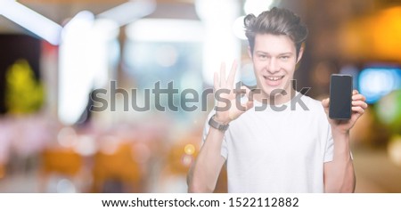 Young man showing smartphone screen over isolated background doing ok sign with fingers, excellent symbol