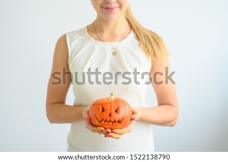 A woman in a white blouse holds a pumpkin for Halloween. Close-up of female hands with a lantern jack on a white background on the eve of All Saints. foreground. Trick or treat. Scary grimace.