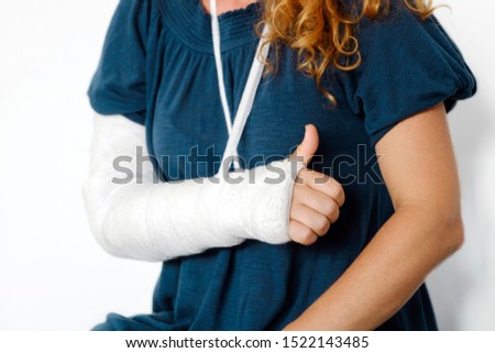 Broken arm in cast and bandage red-haired woman sits on the bed in medical hospital after manipulations of medical worker and shows sign with hand with finger up