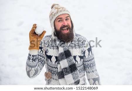 Smiling man snow background. Snow games. Have fun winter day. Cheerful bearded hipster knitted hat and warm gloves play with snow outdoors. Christmas holidays. Making snowball. Happiness concept.