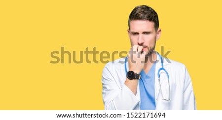 Handsome doctor man wearing medical uniform over isolated background looking stressed and nervous with hands on mouth biting nails. Anxiety problem.