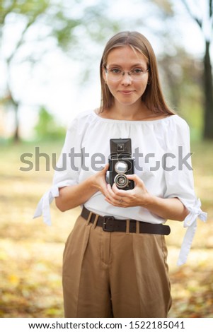 Attractive beautiful young girl holding retro vintage twin lens reflection camera in autumn park. Yellow leaves on the floor and background