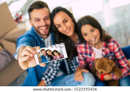 A photo for grandma. Delighted young couple and their kid are taking a joint selfie after moving to the new house.