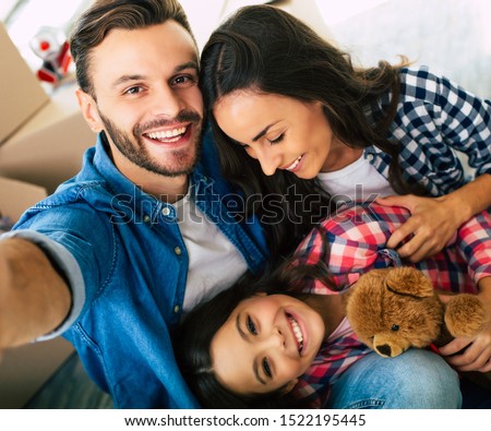 The moment of laughter. Young handsome man with a hollywood smile is sitting on the floor with his family in a new house.
