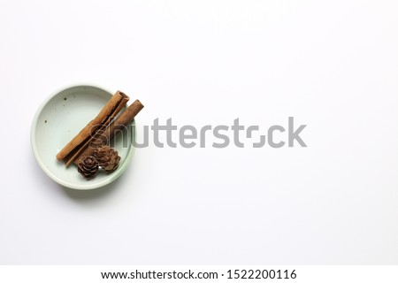 Pine cones and cinnamon sticks in a bowl on white background. Autumn concept