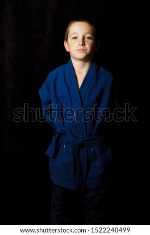 The boy stands on a dark background in a blue kimono, in a rack. Martial arts.