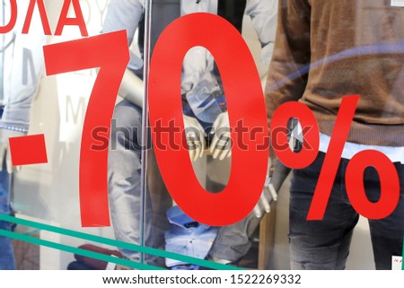 Sale sign 70% percent discount price on stand in shop windows. Season sale, black friday and shopping concept. Clothes on hangers and mannequins in the background.