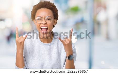 Young beautiful african american woman wearing glasses over isolated background shouting with crazy expression doing rock symbol with hands up. Music star. Heavy concept.