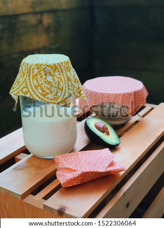 reusable food wraps covering glass jar of milk, bowl and half of avocado. Royalty-Free Stock Photo #1522306064