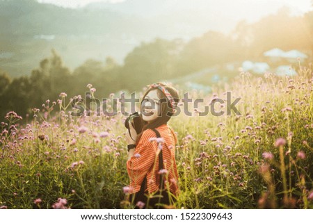 Happy hipster young girl with camera in flower garden. Traveling alone concept.