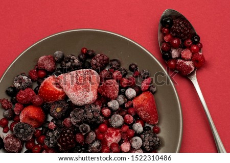 Still life of a plate and a spoon full of red silver fruits like strawberries, raspberries, blueberries
