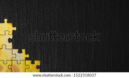 Yellow puzzle on a black stone background. Frame from puzzle around negative space. Royalty-Free Stock Photo #1522318037