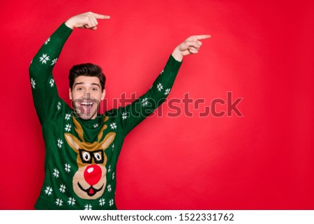 Photo of emotional handsome guy indicating fingers on x-mas sale banner wear trendy knitted green pullover with deer isolated red color background