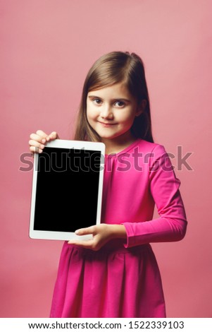 Pretty little girl holding a tablet with a black screen. Pink dress and pink background. Place for text. The concept of special offers for girls, sales, promotions, etc.