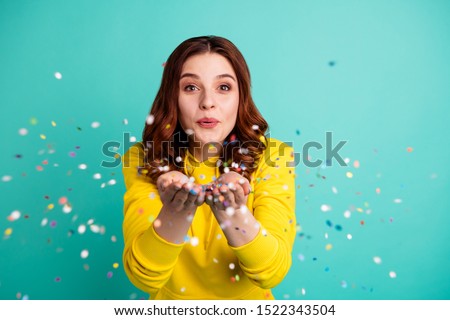 Photo of charming cute fascinating nice young girlfriend blowing confetti at you to show her festive mood with emotional face expression isolated over turquoise vivid color background