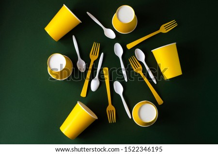 Flat lay yellow and white plastic and paper utensils on a green background. Plastic free concept.