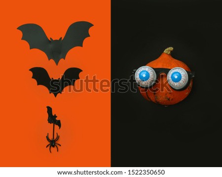 Flat lay Halloween background with pumpkin in in glasses horror symbol eyeball, spider and bats on black backdrop. Festive concept.