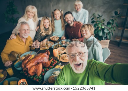 Photo of big family sit hugging feast dishes table around roasted turkey multi-generation relatives grey-haired grandpa making group selfies in living room indoors