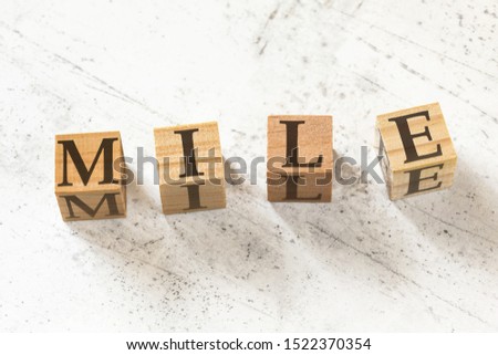Four wooden cubes with letters MILE (meaning Maximum Impact Little Effort) on white working board.