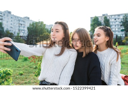 Teenage girls in summer autumn spring in city, take pictures on smartphone, on-line application on Internet video call, girlfriends relax on break at weekend after school