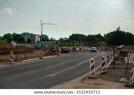 Cars riding on the road works area. Workers are building new road on a summer day.