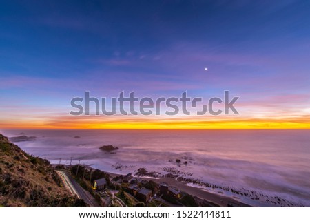 Idyllic scenery at Matanzas beach waves coming from the Pacific Ocean illuminated by a moody sky during twilight. Amazing sea landscape with a colorful sky and a waxing crescent Moon on a starry night