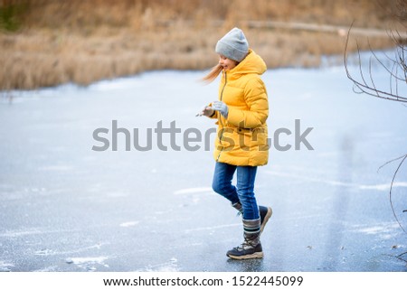 Adorable little girl having fun on frozen lake at late autumn