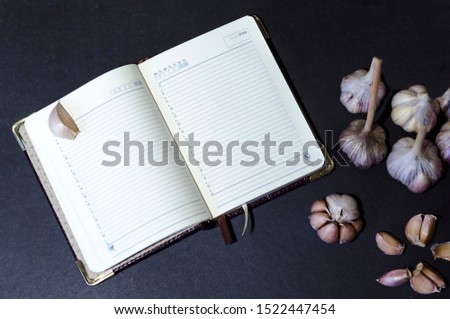 flat lay, top view autumn crop of garlic bulbs, heads of garlic, individual cloves, recipe book, diary on a dark black background. spicy spice, national cuisine. space for text
