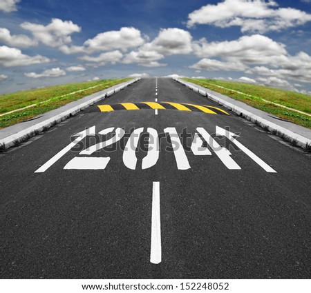 White print arrows and 2014 on an asphalt road, approaching a speed ramp vanishing into the horizon of blue cloudy sky, for the concept of challenges ahead for new year 2014.