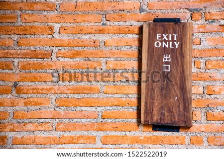 "Exit Only" sign on wooden plank in English and Japanese languages attached to orange brick wall.