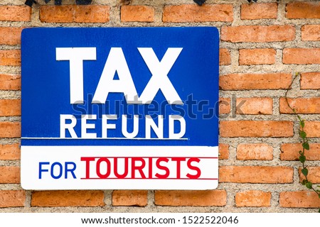 "Tax Refund for tourists" sign in white letters on blue background attached to orange brick wall.