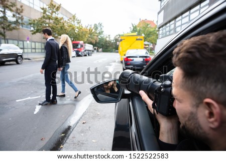 Young Male Spy Sitting In The Car Taking Photograph Of A Couple Walking On Street Royalty-Free Stock Photo #1522522583