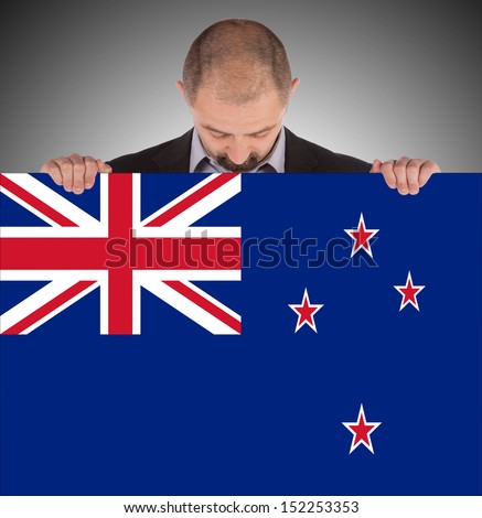 Smiling businessman holding a big card, flag of New Zealand, isolated on white