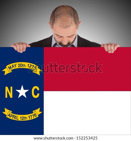 Smiling businessman holding a big card, flag of North Carolina, isolated on white