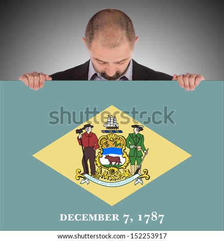 Smiling businessman holding a big card, flag of Delaware, isolated on white