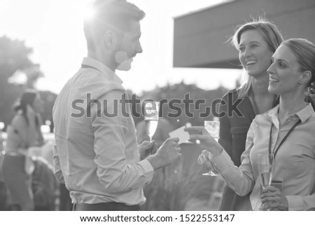 Black and white photo of Young businesswoman giving business card to colleague while holding wine glass on success party at rooftop