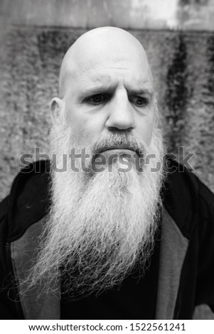 Sad mature bald man with long gray beard thinking against concrete wall outdoors
