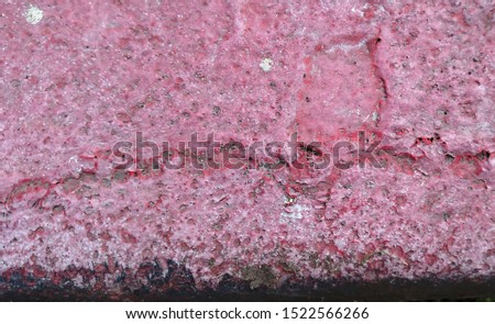 Patterns of cracks in the weathered red paint on the curb of a city street